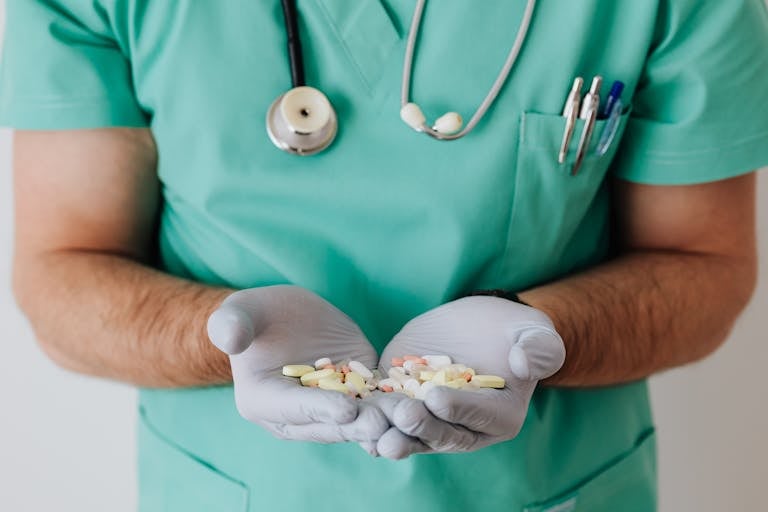 A healthcare professional in uniform holding a variety of pills in gloved hands.